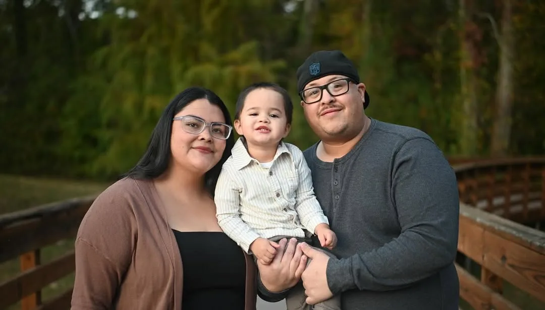 Parents holding their toddler on a wooden bridge at a park