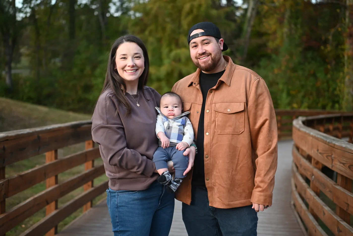 Parents holding their baby on a wooden boardwalk surrounded by trees
