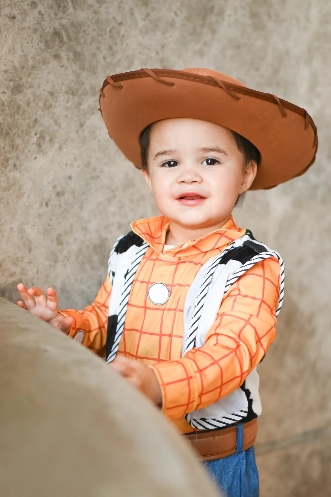 A toddler in a cowboy hat and Toy Story costume smiling during a session
