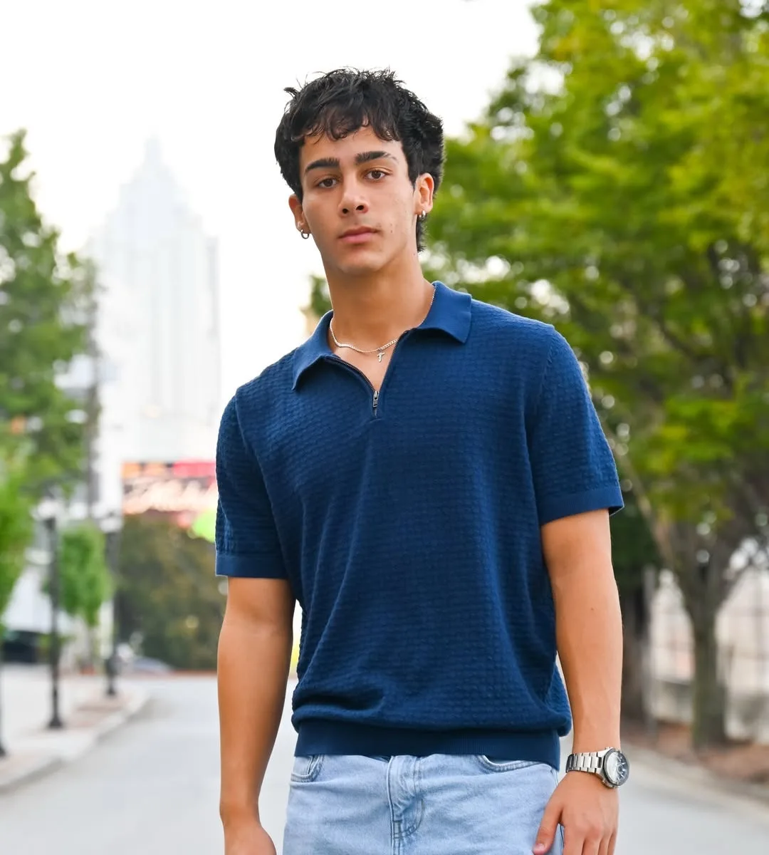 A young man in a blue knit polo standing on a quiet city street