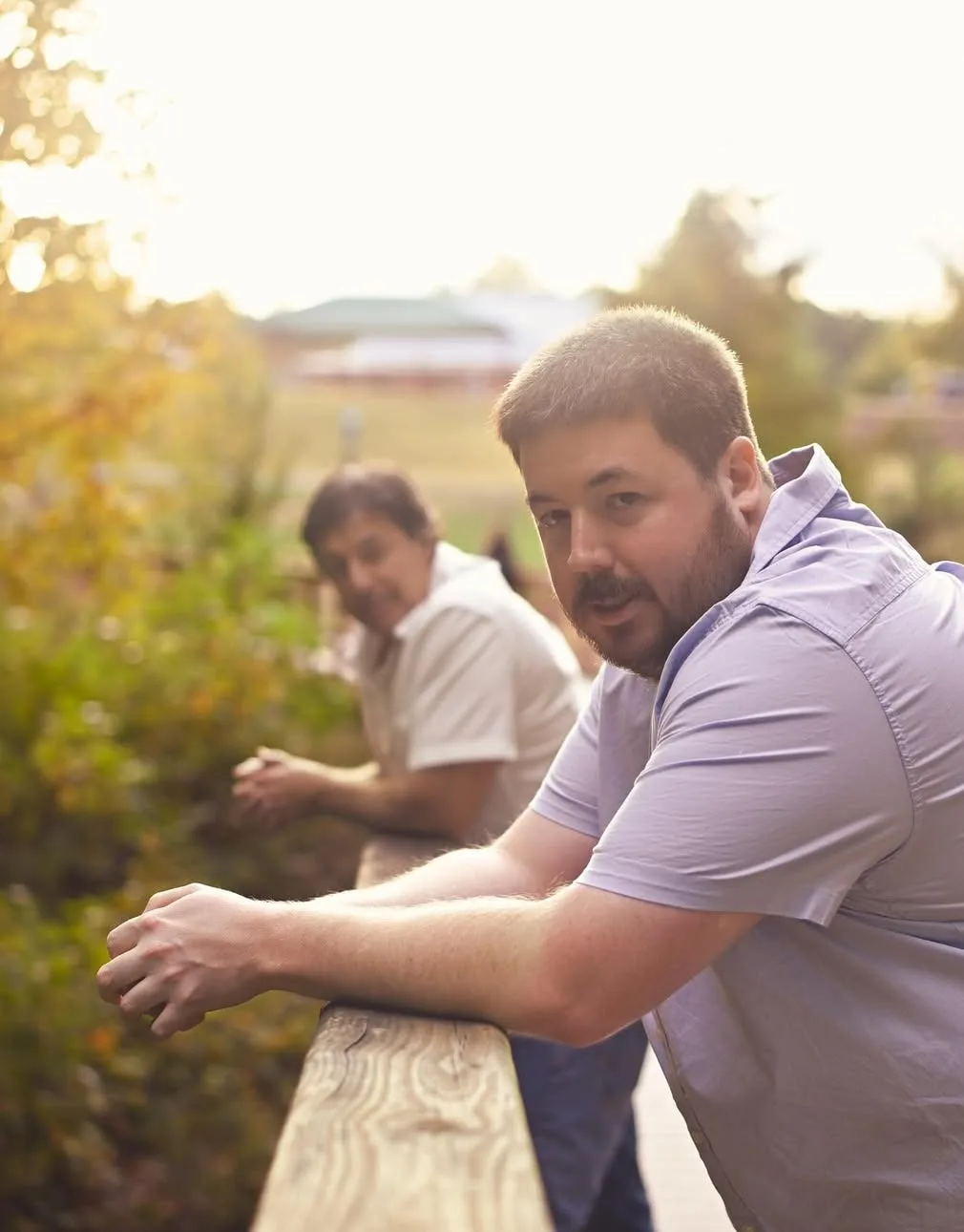 Two men talking at a wooden railing in warm evening light