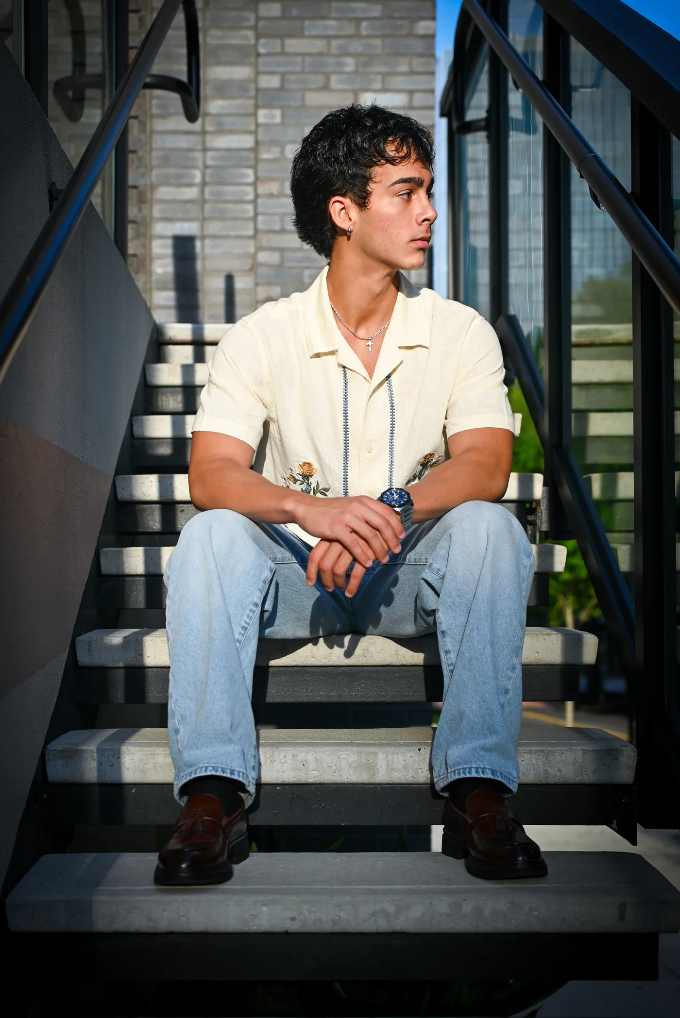 A young man in a cream button-up sitting on concrete stairs with sunlight falling across him